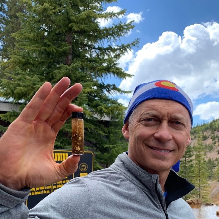a man smiling for the camera holding up the gold he found while gold panning with country boy mine in breckenridge, colorado