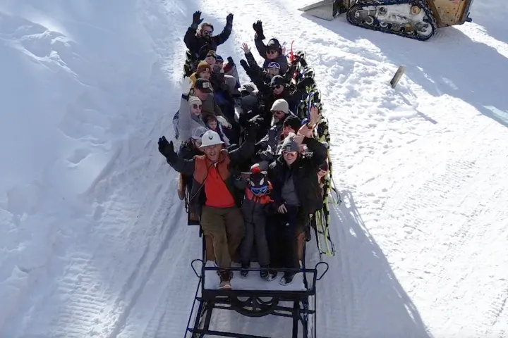Group of people on a snow-covered sled ride, waving at the camera.