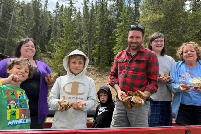 Group of people outdoors holding large rocks, surrounded by trees.
