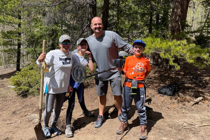 Group of four people with metal detector in a forest setting.