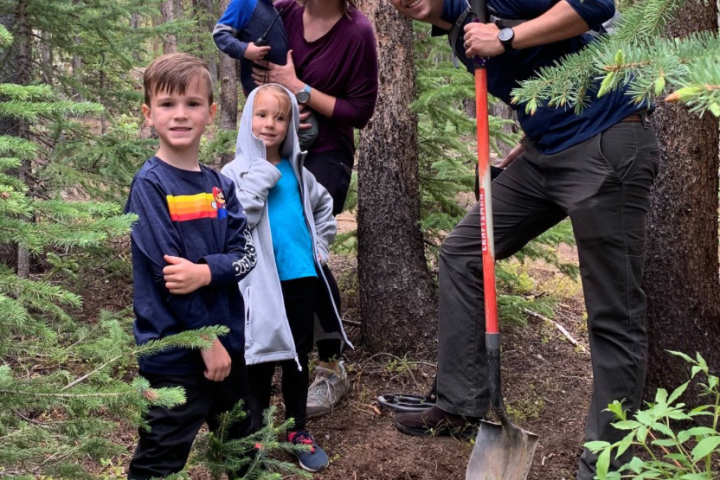 Family with three children and a shovel standing in a forest clearing.