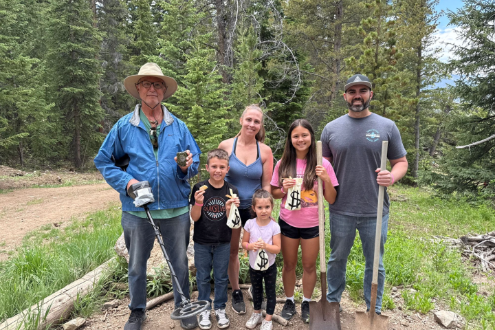 Family with shovels and metal detector in a forest clearing.
