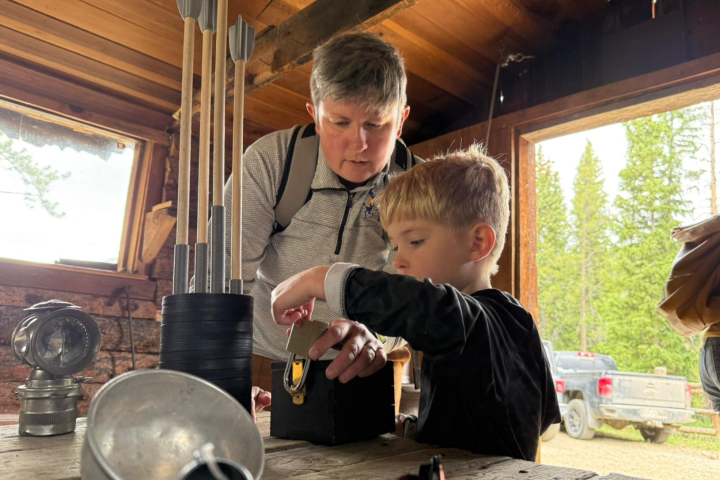 Adult helping child with a wooden project inside a rustic cabin.
